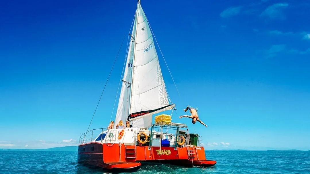 Sailing catamaran with tourists in Whitsundays, person diving into the sea.
