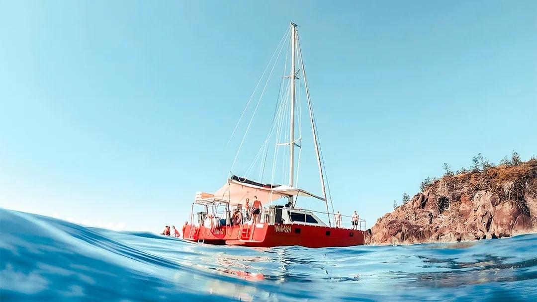 Catamaran sailing near rocky shore in Whitsundays, Australia.