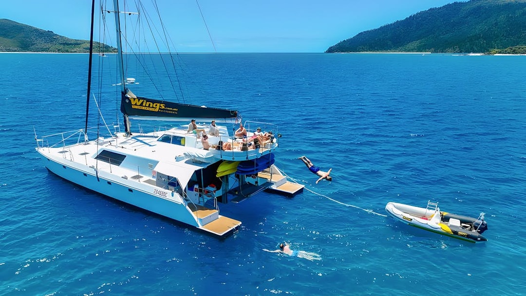 Tourists enjoying a catamaran tour in the Whitsundays, with one diving into the sea.