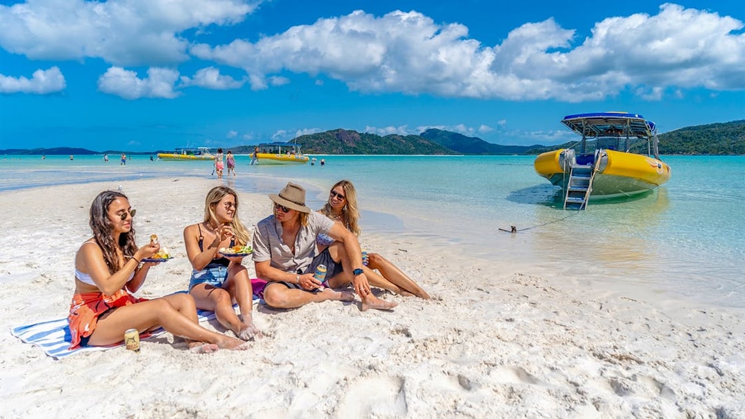 Group relaxing on Whitehaven Beach with a yellow boat in the Whitsundays, Australia.