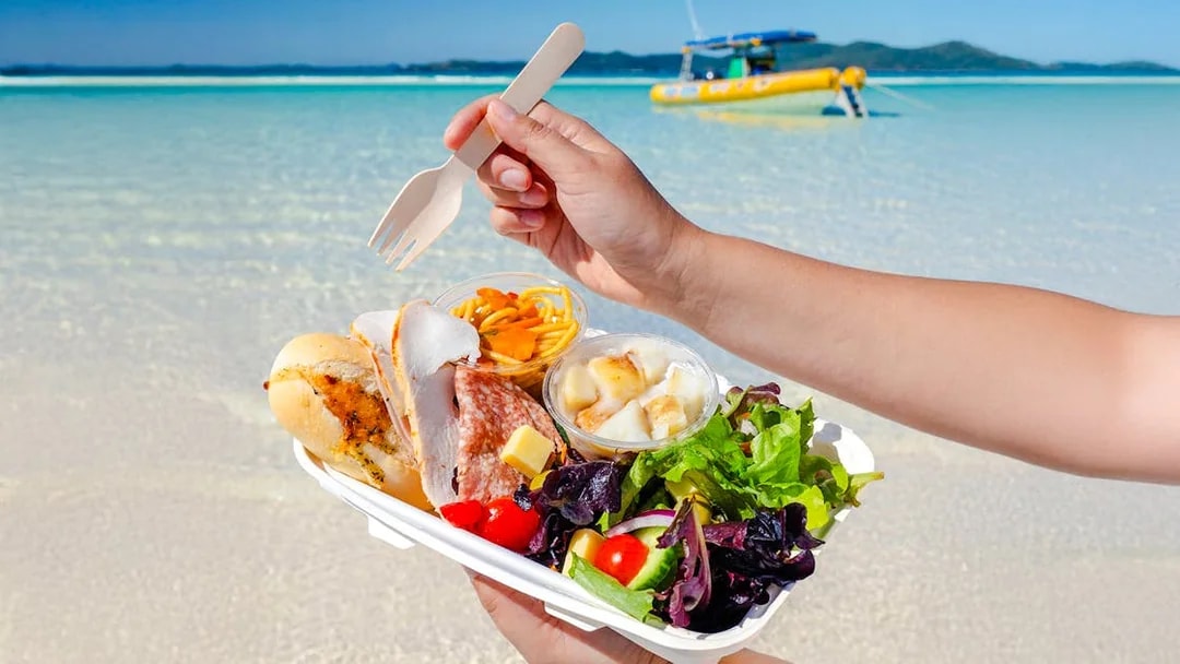 Lunch served on Whitsundays beach with a boat in the background.