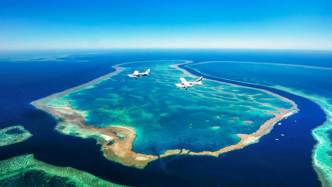 Aerial view of Whitsundays coral reefs with two planes flying over turquoise waters.