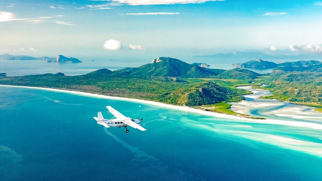 Aerial view of Whitsundays with a plane flying over turquoise waters and lush islands, Australia.