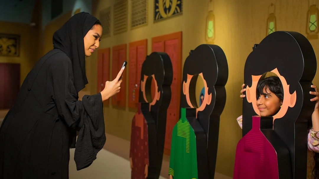 Visitor photographing child posing with cutout at Al Shindagha Museum.