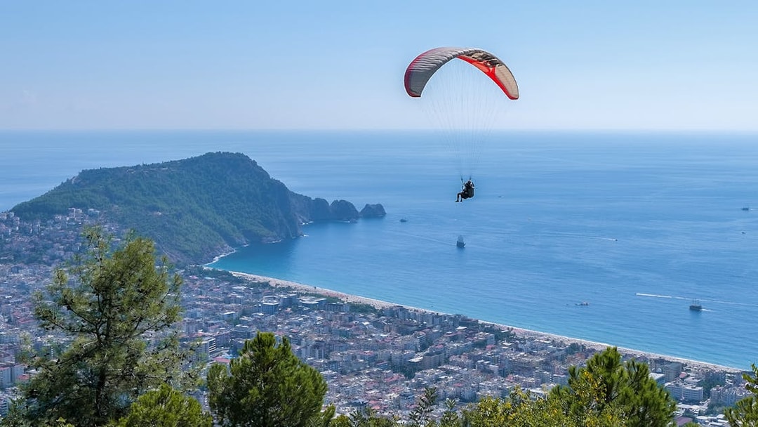 Paraglider soaring over Alanya coastline with city and sea view.
