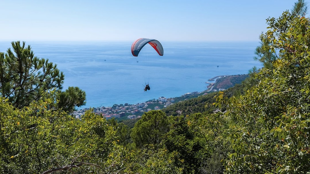 Paraglider soaring over Alanya coastline with sea and forest views.