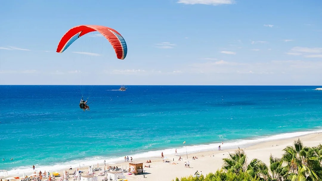 Paragliders soaring over Alanya beach with turquoise sea in the background.