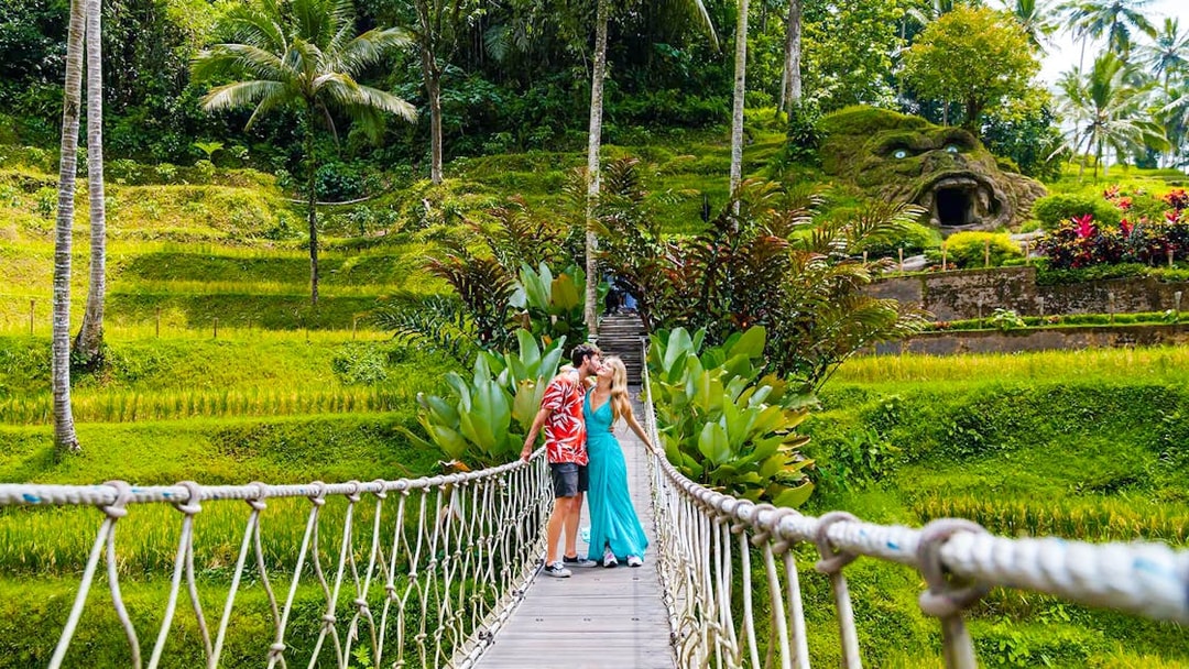 Couple kissing on a suspension bridge at Alas Harum, Bali, surrounded by lush greenery.