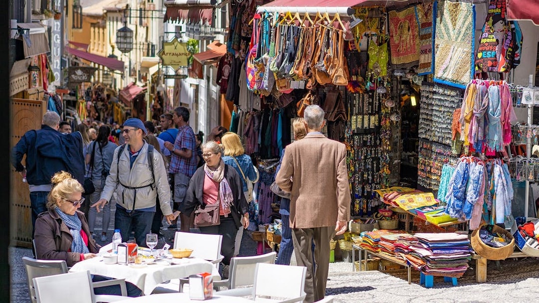Street market in Albaicin, Granada, with tourists exploring shops and outdoor cafes.
