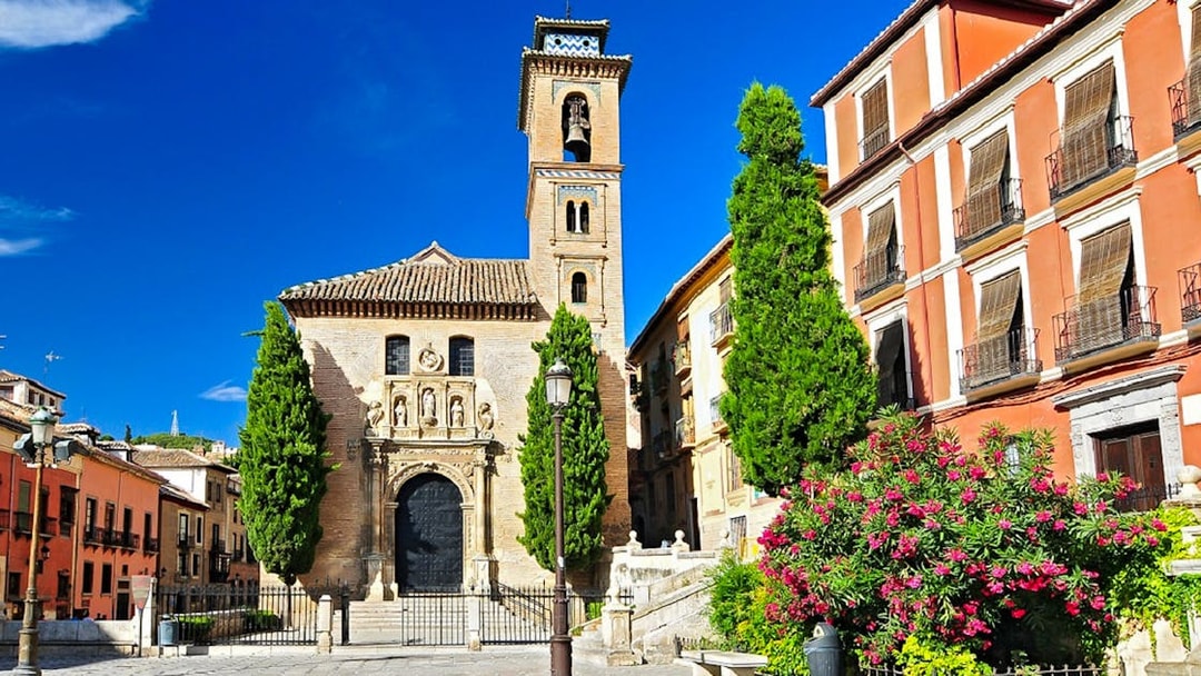 Historic church facade in Albaicin, Granada, with bell tower and vibrant flowers.