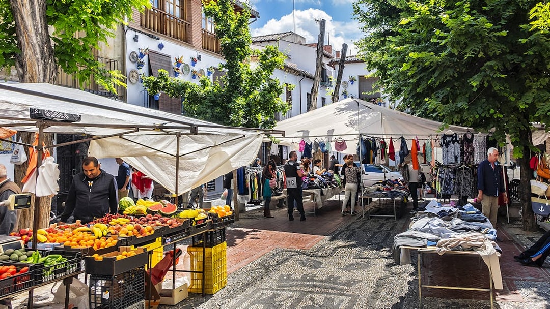 Outdoor market in Albaicin, Granada with stalls selling fruits, clothes, and local crafts.