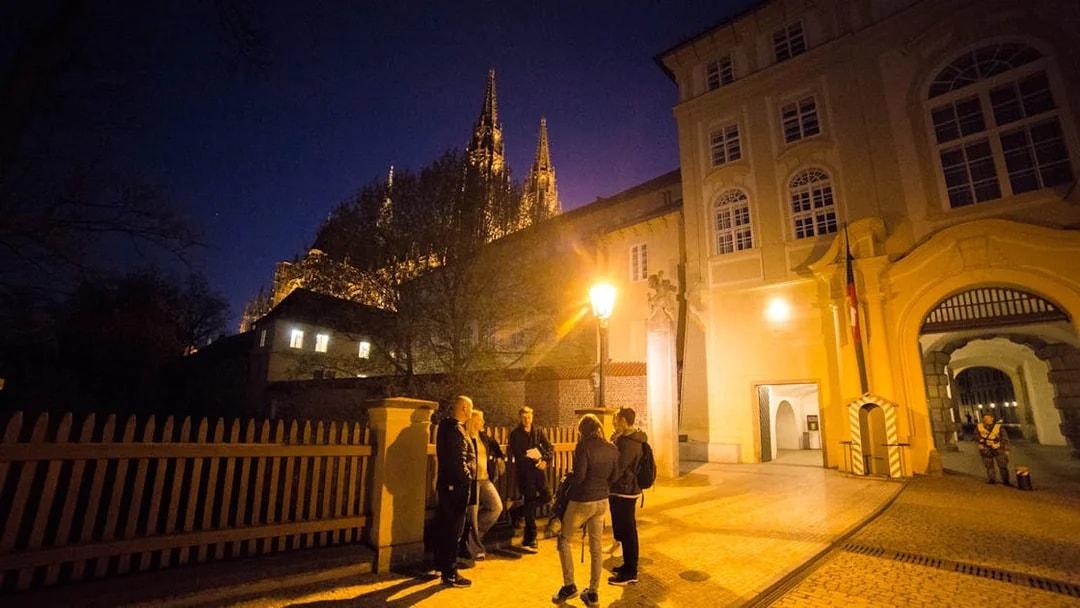 Group of people on a night tour near Prague Castle, illuminated spires in background.