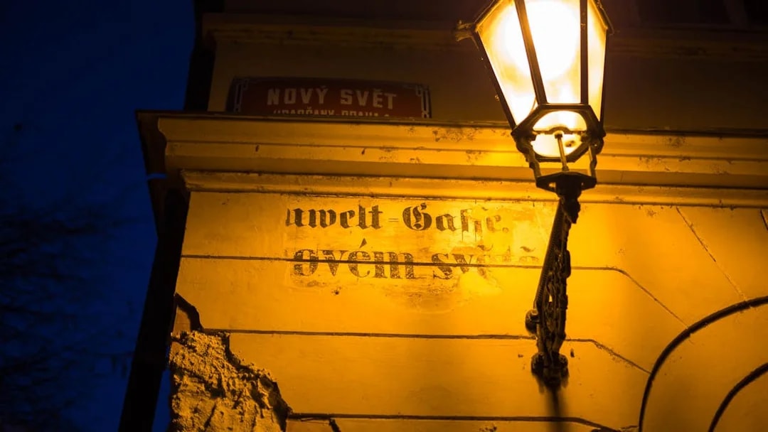 Street lamp illuminating a wall with faded text in Nový Svět, Prague.