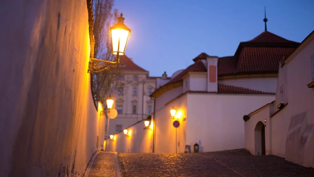 Cobblestone street with lanterns at dusk near Prague Castle.