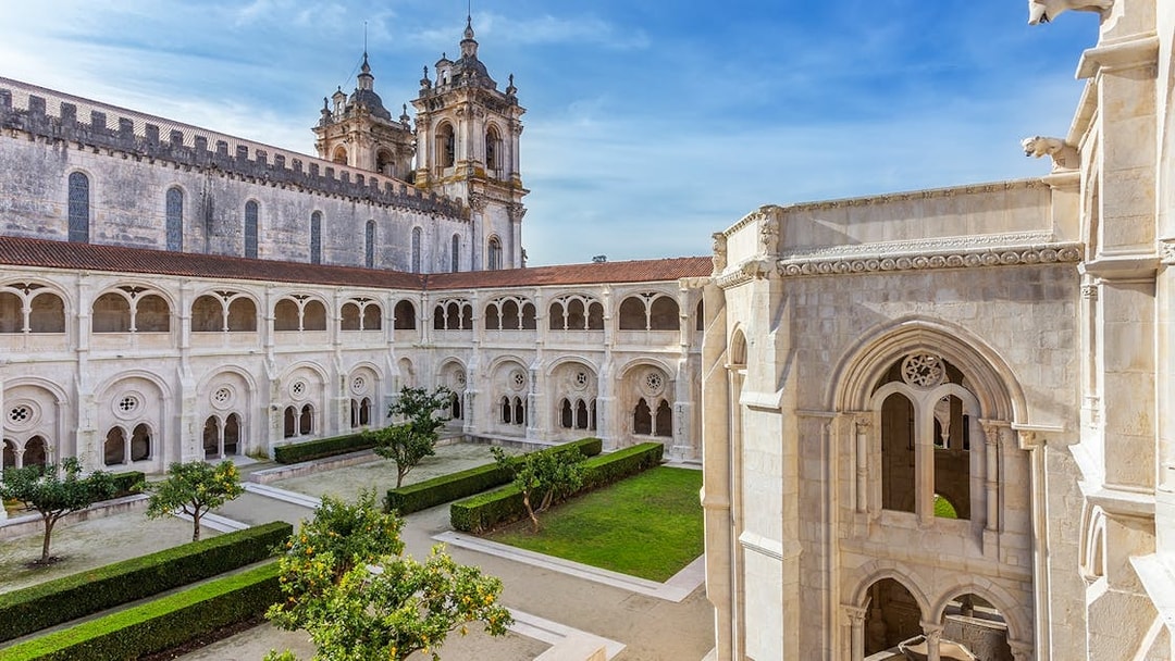 Alcobaça Monastery courtyard with Gothic architecture and manicured gardens in Portugal.