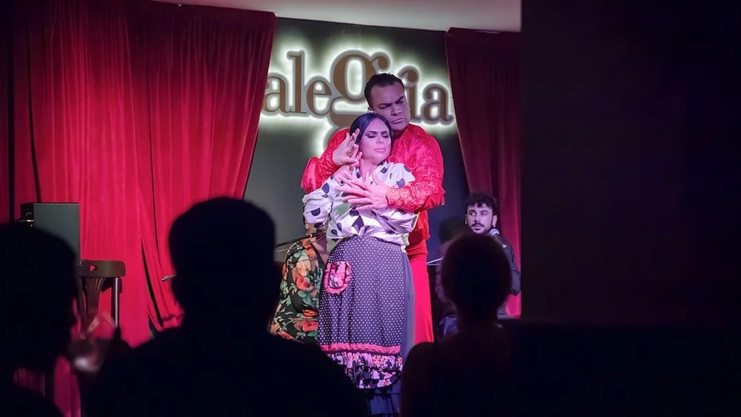 Flamenco dancers performing at Alegría with red curtains in the background.