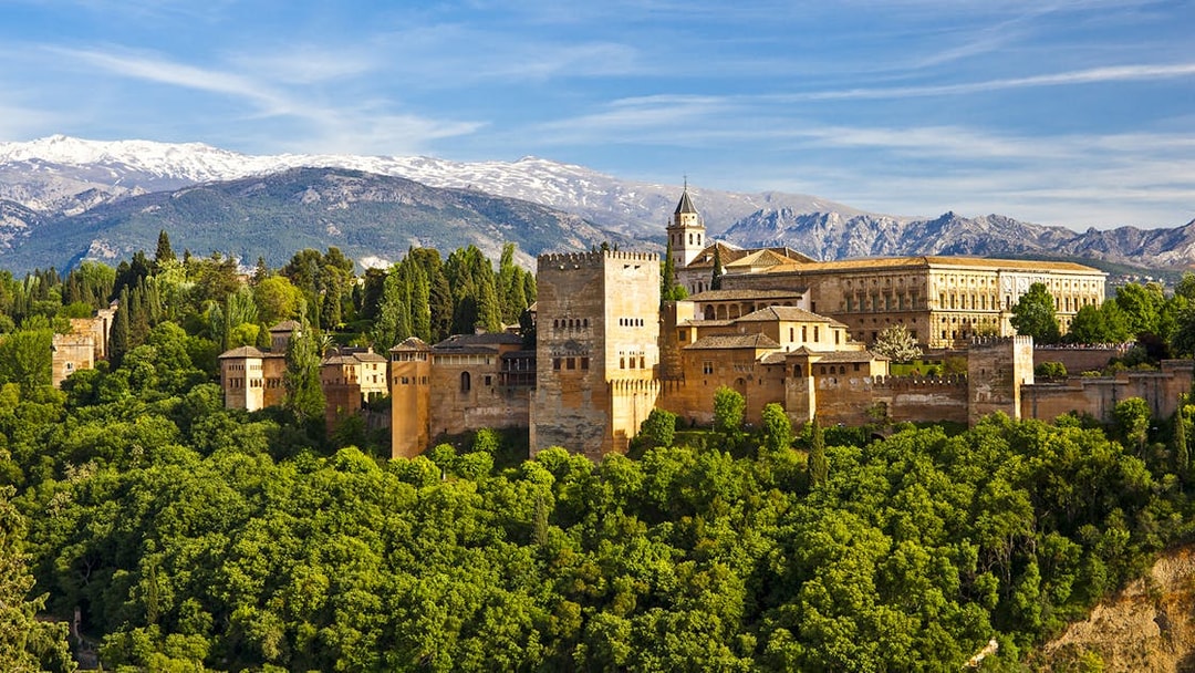 Alhambra palace and Generalife gardens in Granada, Spain, with Sierra Nevada mountains in the background.
