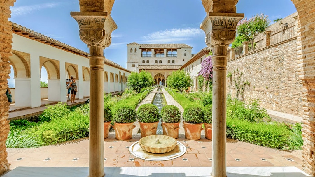 Courtyard view of Alhambra's Nasrid Palaces with arches, gardens, and central fountain in Granada, Spain.