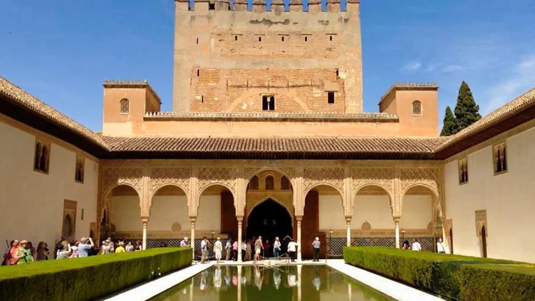 Visitors at Alhambra's Nasrid Palaces courtyard with reflecting pool, Granada, Spain.