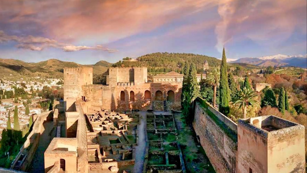 Alhambra fortress with Nasrid Palaces in Granada, Spain, surrounded by lush greenery and mountains.