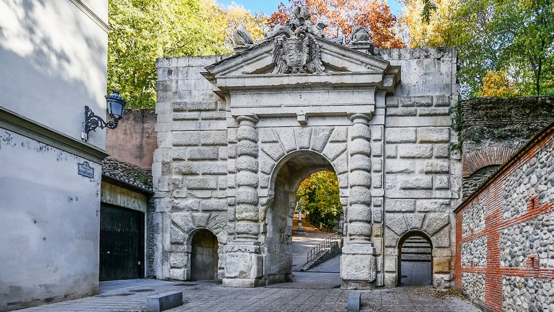 Gate of the Pomegranates entrance at Alhambra, Spain, with stone archway and surrounding trees.