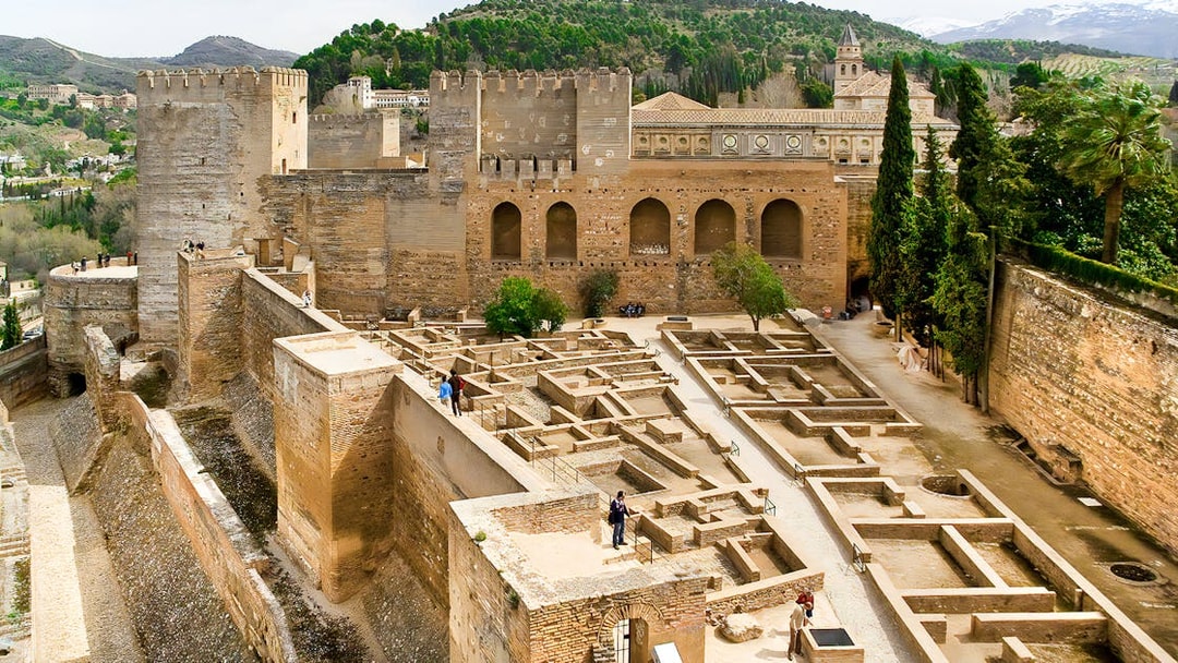 Alhambra fortress walls and ruins in Granada, Spain, with surrounding hills.