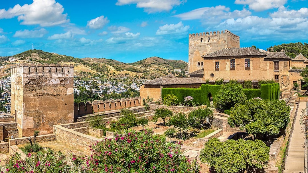Alhambra fortress gardens and towers in Granada, Spain, with scenic hillside view.