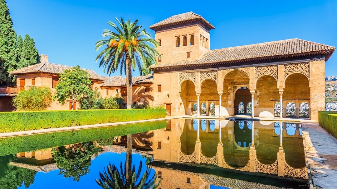 Alhambra palace reflecting in pool on a sunny day in Granada, Spain.