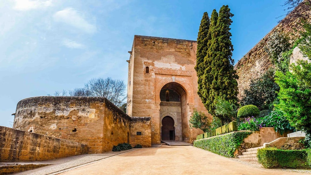 Alhambra entrance with stone walls and lush greenery, Granada, Spain.