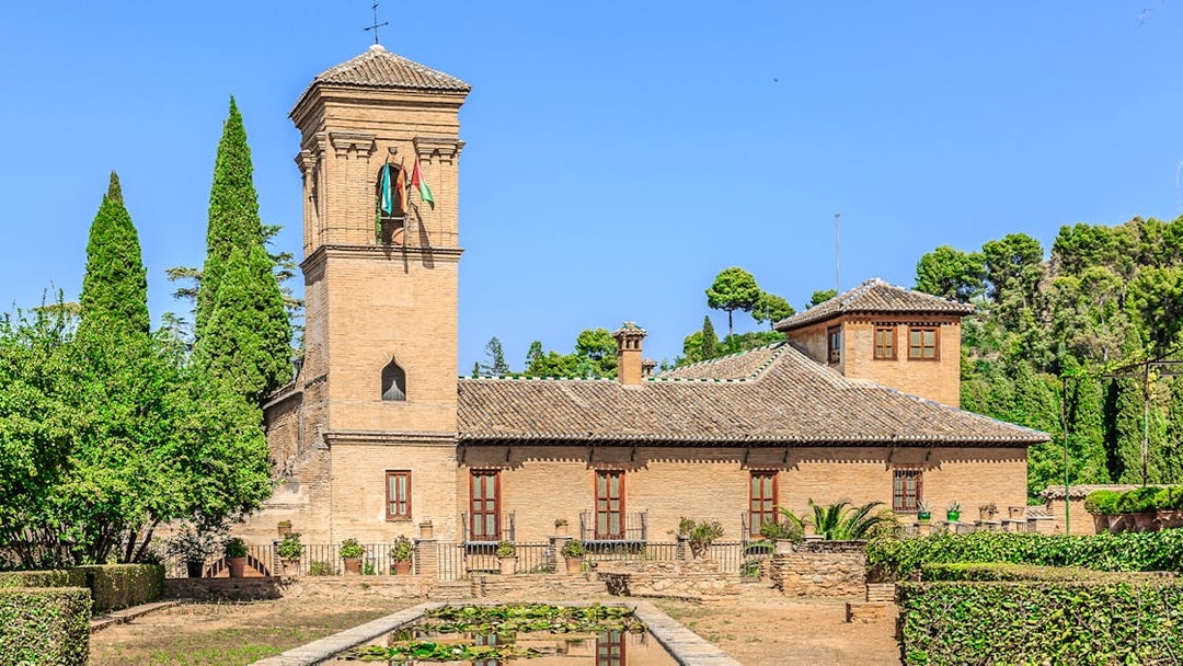Alhambra tower and gardens with lush greenery under a clear blue sky.
