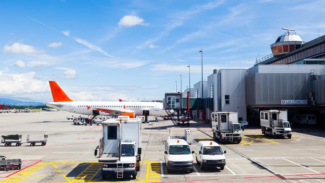 Airplane on runway at Geneva Airport with service vehicles nearby.