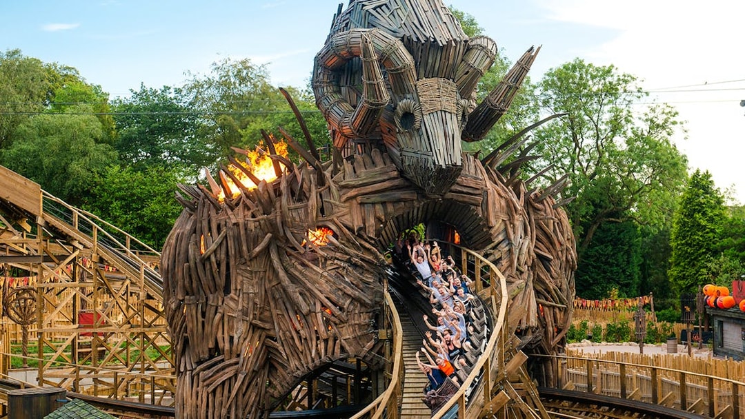 Riders on The Wicker Man roller coaster at Alton Towers, passing through a wooden structure with flames.