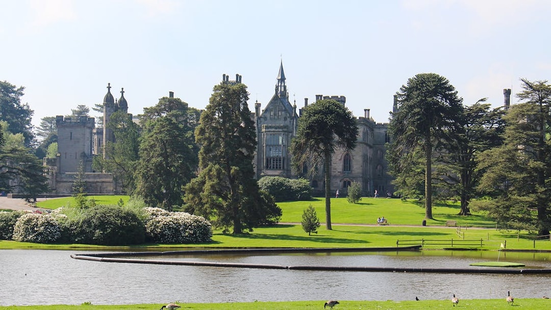 Exteriors of Alton Towers with lush gardens and a serene pond in the foreground.