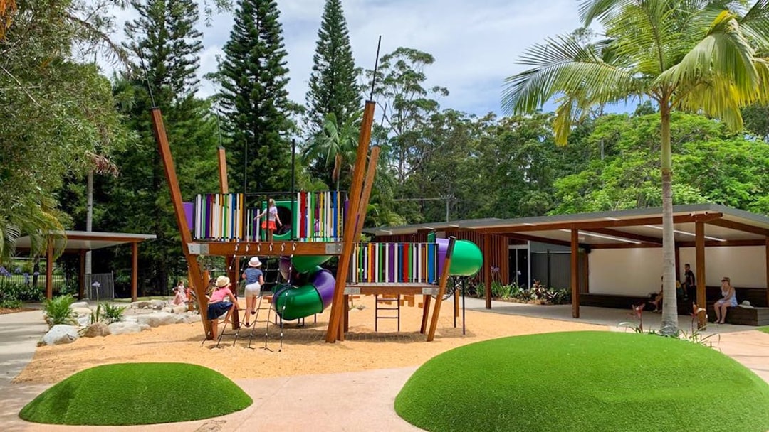 Children playing on colorful playground equipment at Amaze World, surrounded by trees and greenery.