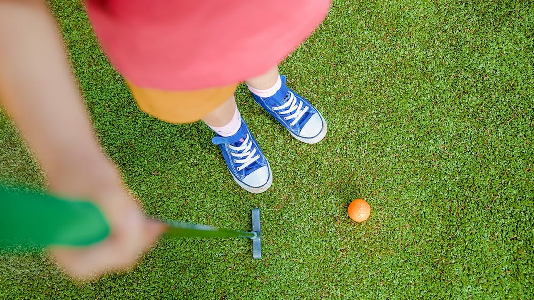 Girl aiming to putt orange ball on mini golf course.