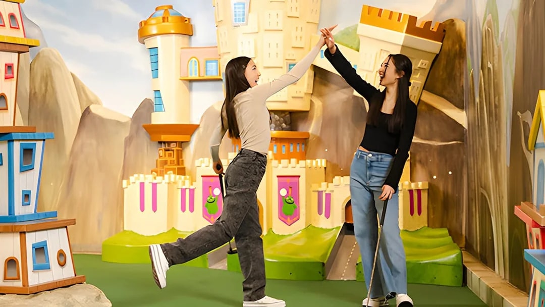 Two people high-fiving at Angry Birds Mini Golf, American Dream, with colorful castle backdrop.