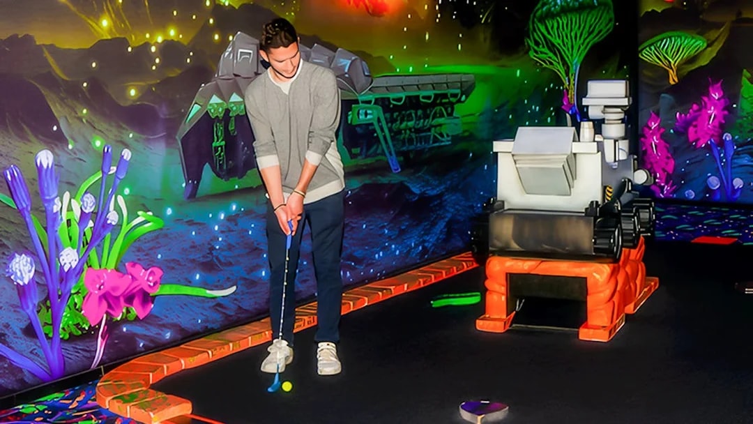 Blacklight mini golf course with guest putting near neon space-themed decor.