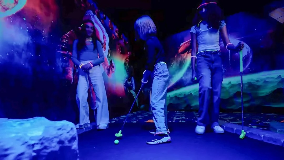 Guests playing mini golf under blacklight with glowing murals.