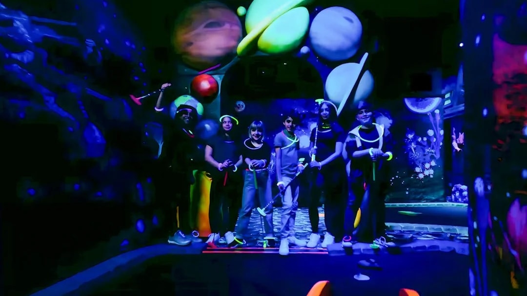 Guests playing blacklight mini golf with glowing planets in the background.