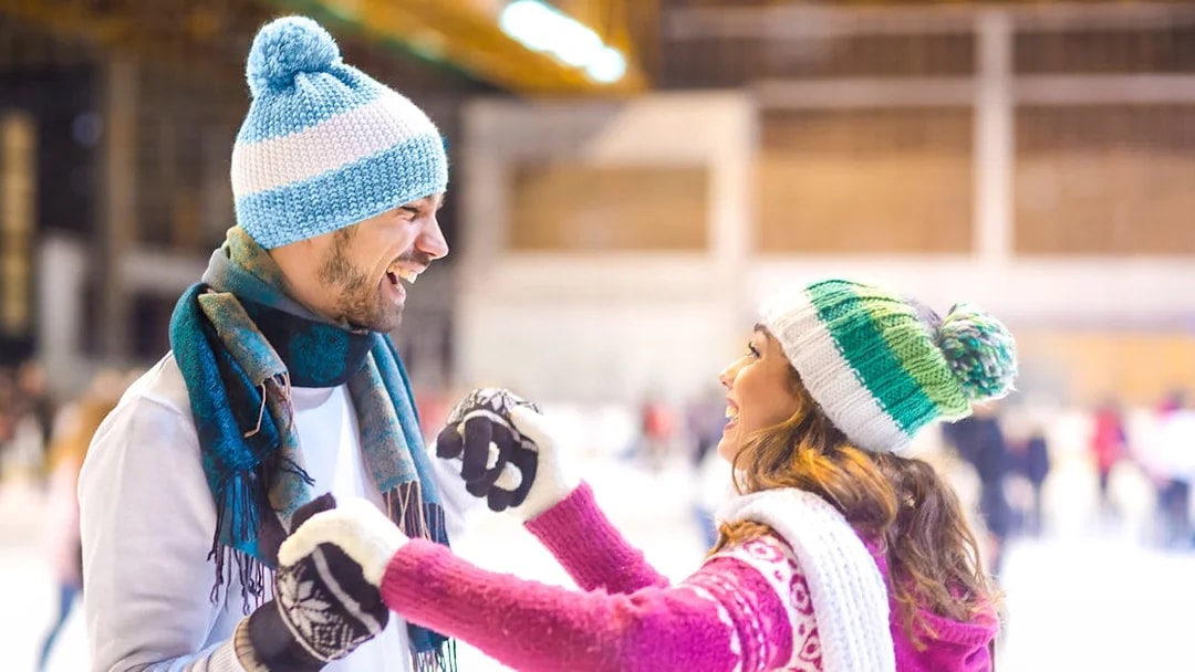 Young couple laughing while ice skating indoors.