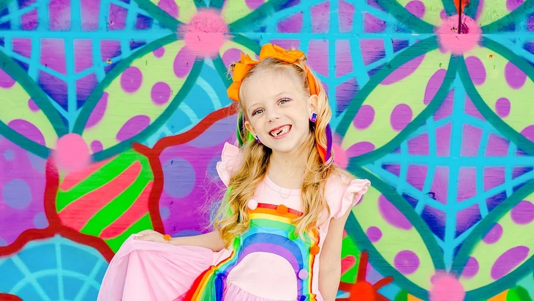 Girl smiling in front of a colorful geometric mural.