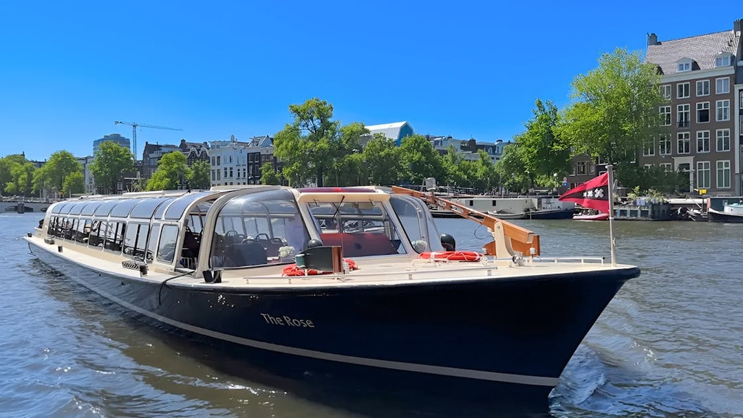Tour boat cruising Amsterdam canal with historic buildings in the background.