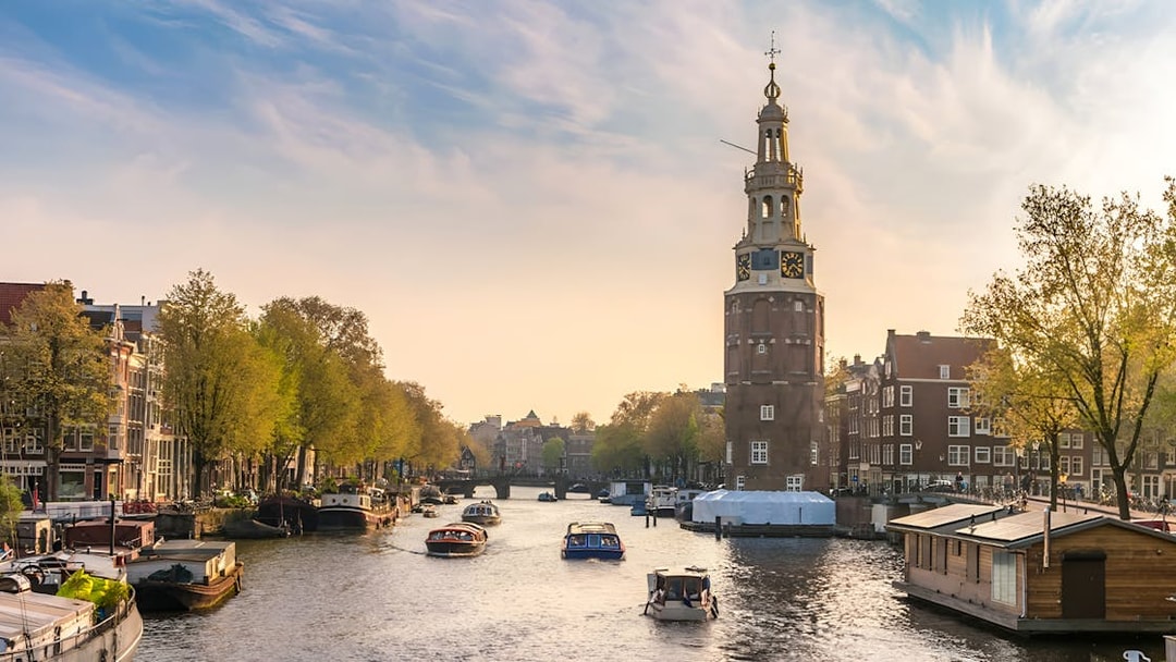 Amsterdam canal with tour boat passing historic buildings and Montelbaanstoren tower.