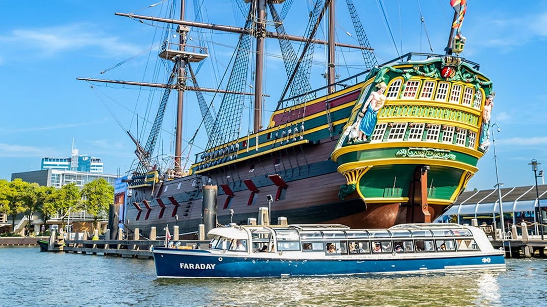 Canal cruise boat passing a historic ship in Amsterdam harbor.