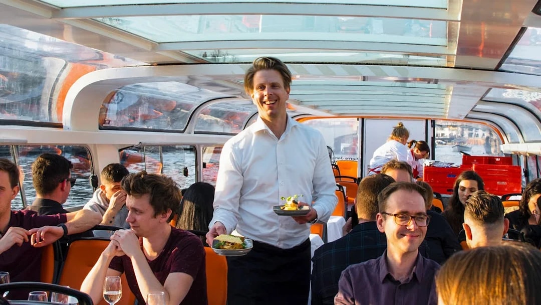 Service staff serving meals on a dinner cruise boat with guests dining.