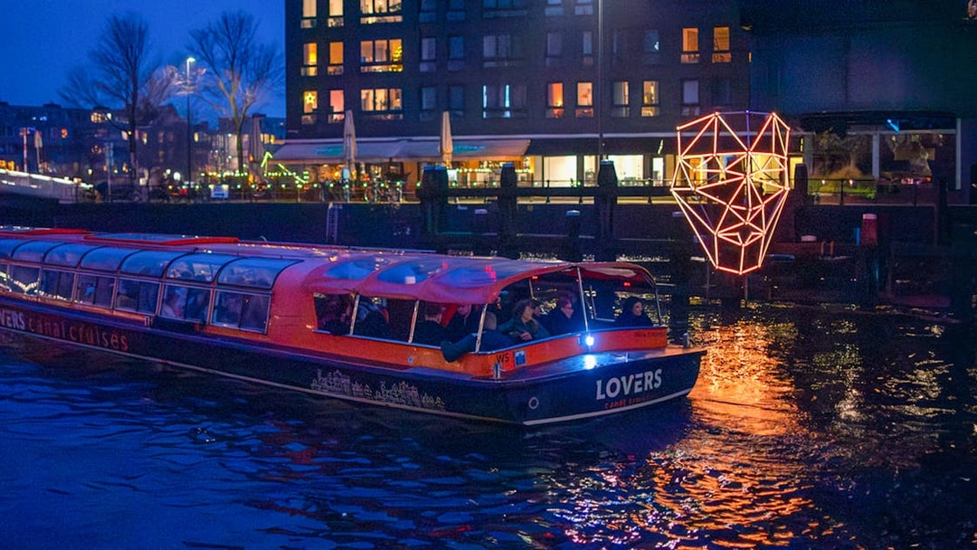 Amsterdam canal boat with passengers on a dinner cruise at night, illuminated by city lights.
