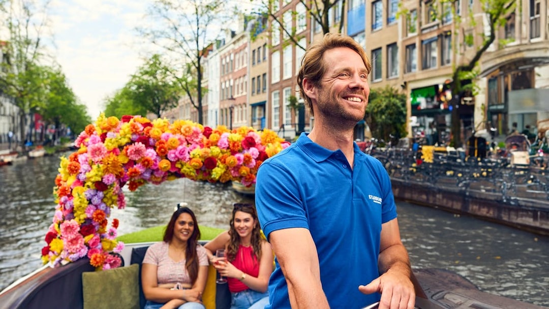 Amsterdam canal cruise on a flower-adorned boat with smiling passengers.