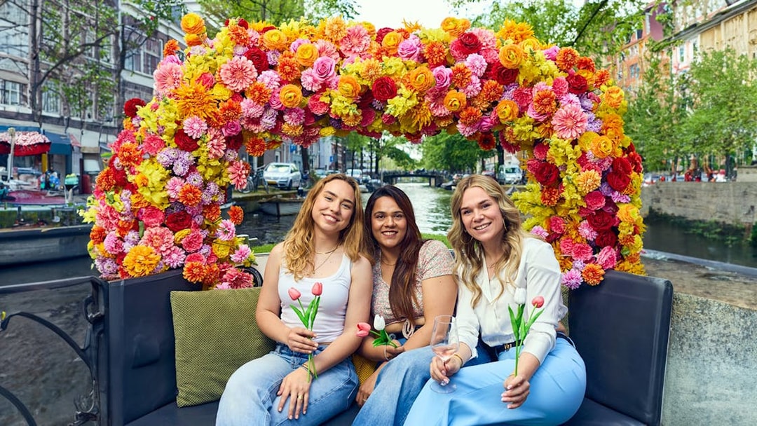 Three people holding tulips on a flower-adorned boat during an Amsterdam canal cruise.