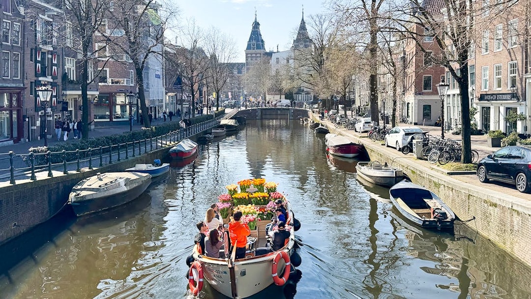 Boat with tulips sailing through Amsterdam canal with historic buildings.