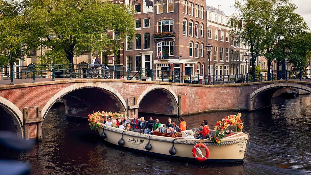 Luxury canal cruise on flower-adorned boat passing under Amsterdam bridge.